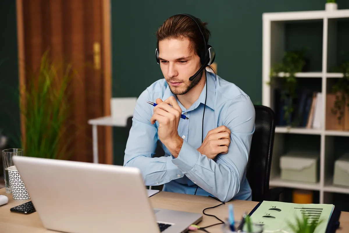 Customer support agent wearing a headset, working at a laptop in an office