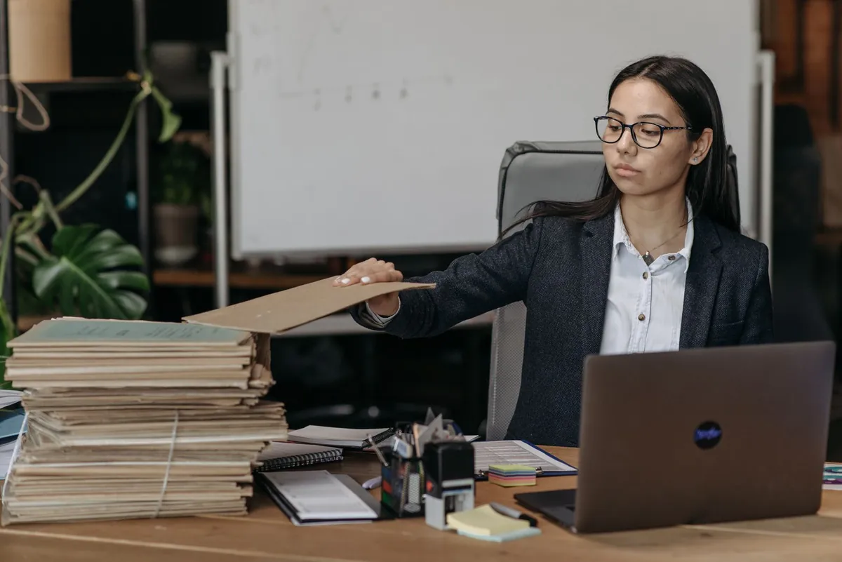 Businesswoman organising files beside a laptop, the required format of an llms.txt file